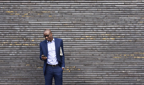 man using mobile phone leaning against wall 470x280