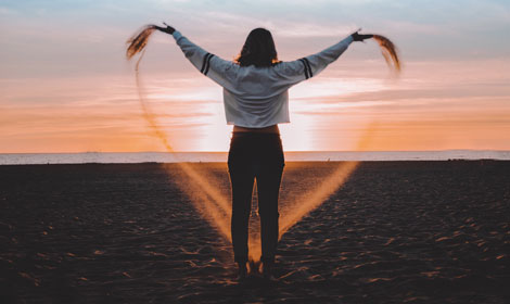 woman forming heart with sand on beach 470x280